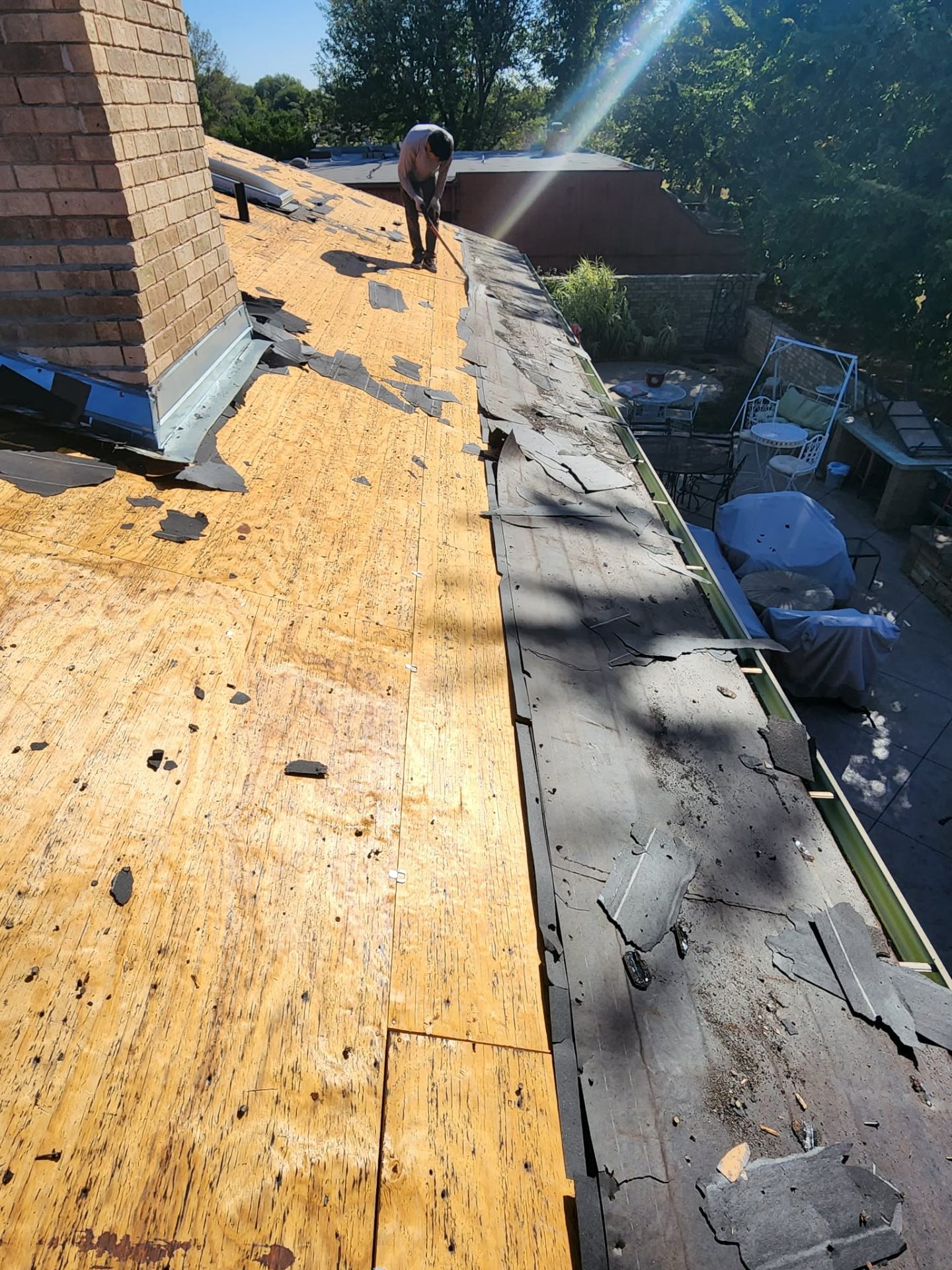 Tear-off in progress around brick chimney β exposed decking